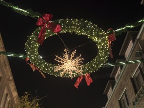 Illuminated Christmas wreath with lights and decoration above a street at night, bocholt,