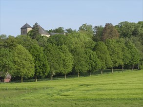 A church is located in the middle of a green forest bordering extensive fields, the atmosphere is