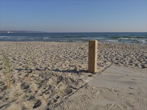 Beach with sand, calm waves and wooden posts under a sunny blue sky, Binz, Rügen, Germany, Europe