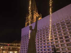 Statue in front of an illuminated church at night with fairy lights creating a festive atmosphere,