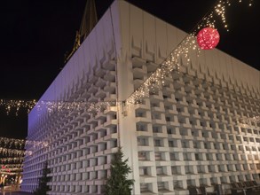 A modern building with Christmas decorations and fairy lights, suspended red ball, at night, Ahaus,