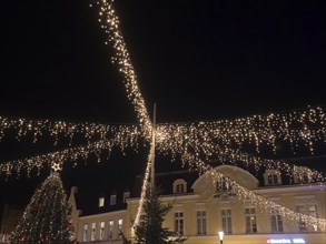 Festively illuminated scenes at night with fairy lights above a building and Christmas decorations,