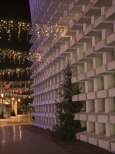 Modern buildings with Christmas lighting and a Christmas tree along a festively illuminated street,