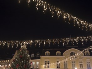 Atmospheric Christmas scene with fairy lights over a square and a Christmas tree in front of it,