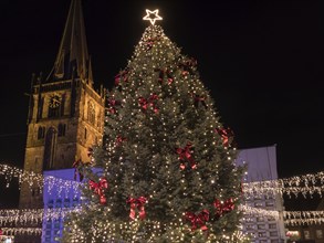 Large Christmas tree with lights and red bows, illuminated by a shining star, next to a church at