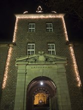 Brick entrance area of a district court with illuminated arch and fairy lights at night, Ahaus,