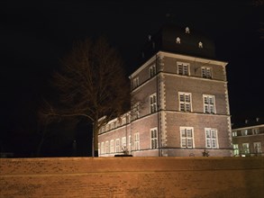 Historic brick building at night with lighting and a bare tree in the foreground, Ahaus,