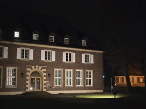 A large historic building illuminated at night, with many windows and a small lawn in front of it,