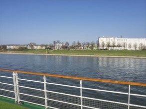 View from a ship's railing onto a river and apartment blocks in an urban environment, Cologne,