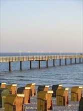 Beach chairs in different colours line the beach with a long jetty jutting out into the sea, Binz,