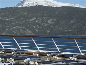 Sun loungers on the deck of a cruise ship overlooking snow-capped mountains and a tranquil fjord,