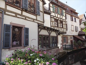 Charming, historic half-timbered house on a canal with unrendered shutters and flowering plants,