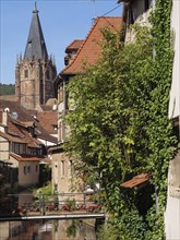 Half-timbered houses by the river under a blue sky, a church in the background, Wissembourg,