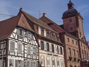 Traditional half-timbered houses and a baroque building in a French town under a clear sky,