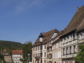 Town view with half-timbered houses and mountainous landscape in the background under a blue sky,