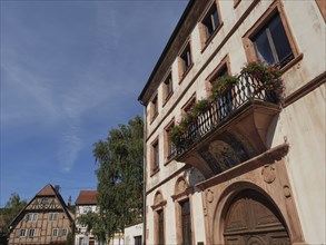 Historic building with balcony and flower boxes under a blue sky in a town, Wissembourg, Alsace,