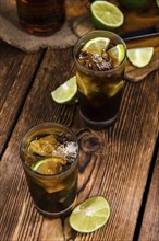 Cuba Libre longdrink with pieces of fresh lime and crushed ice on wooden background