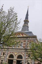 Historic church tower rises above an ornate building view into the cloudy spring sky, The Hague,