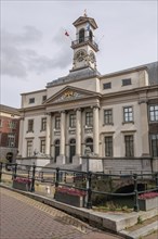 Historic town hall with columns and clock tower, adjacent to a paved pedestrian zone and flower