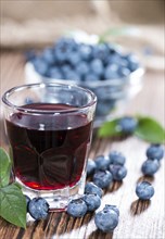 Blueberry Liqueur in a shot glass (on wooden background)