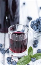 Blueberry Liqueur in a shot glass (on wooden background)