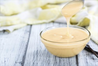 Vanilla Sauce in a small bowl (close-up shot) on wooden background