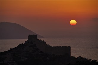 Castle ruins as a silhouette at sunset with a view of the sea and mountains, dark sky, Kritinia