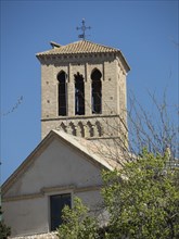 Church bell tower with stone masonry, surrounded by trees, with clear sky and spring-like flair,