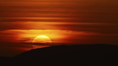 A dramatic sunset behind a hill that bathes the sky in deep red-orange tones, offshore island,