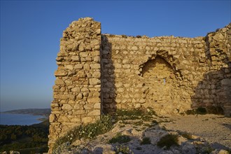 A historic stone ruin on a hill overlooking the sea and vegetation, Kritinia Castle, St John's