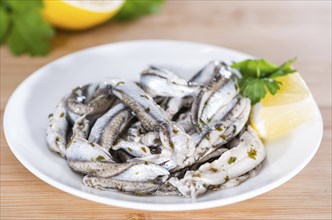 Pickled Anchovis with herbs (close-up shot) on wooden background