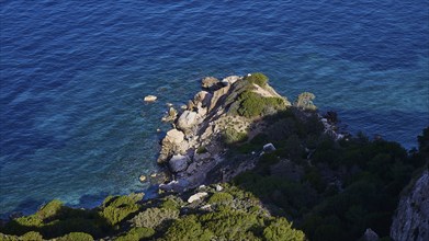 View from above of the rocky coastline where the blue sea meets the cliffs, surrounded by green