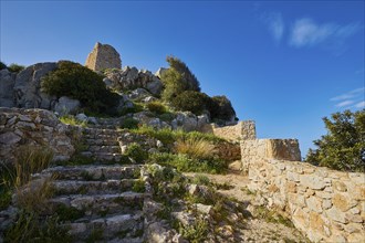 Stone steps lead to the ruins of an ancient castle, surrounded by nature under a blue sky, Kritinia