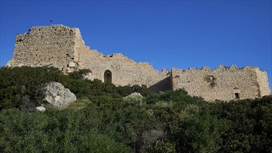 Ruins of an old building under a clear blue sky, surrounded by green overgrown grounds, Kritinia