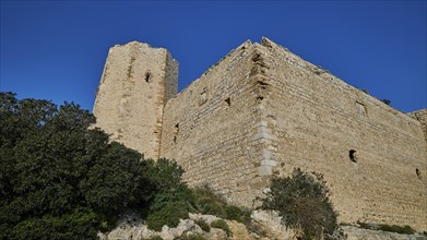 Corner of a castle ruin with massive stone tower, sparse vegetation, under a clear blue sky,