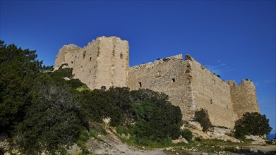 Ruins of a large castle complex, surrounded by dense vegetation and a clear blue sky, Kritinia