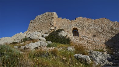 Ruins of a castle with partially preserved walls and a window, surrounded by vegetation under a