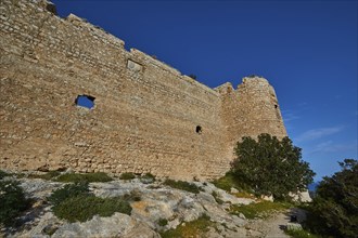 Side view of an old castle with thick stone walls and sparse vegetation under a clear sky, Kritinia