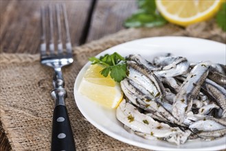 Pickled Anchovis with herbs (close-up shot) on wooden background