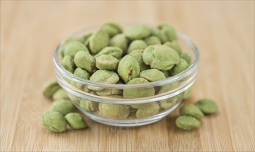 Wasabi coated Peanuts as high detailed close-up shot on a vintage wooden table (selective focus)