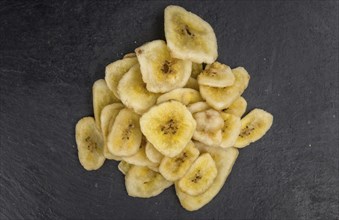 Some Dried Banana Chips on a slate slab as detailed close-up shot, selective focus