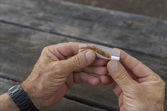 Close-up view of a man's hands rolling a cigarette on a wooden table