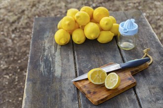 Top view of a lemon cut with a knife on a wooden board in the background pile of lemons and a