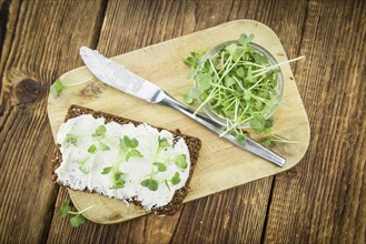 Slice of wholemeal bread with fresh cutted cress and cream cheese on an old wooden table (selective