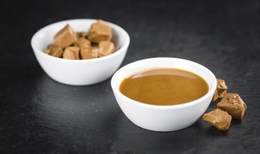 Portion of Caramel Sauce as detailed close up shot on a slate slab (selective focus)