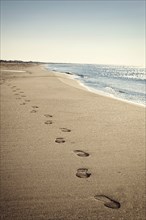 Coastal landscape with thin beach and blue sea, footsteps in sand