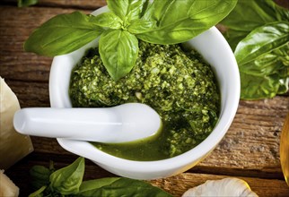 Homemade pesto sauce with basil and pine nuts in white mortar over old wooden table