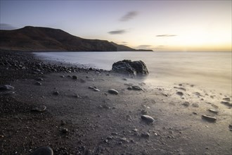 View of the sunrise over the Atlantic. A coastline and a bay with a rocky beach on a volcanic