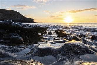 View of the sunrise over the Atlantic. View over a stone beach on a volcanic island. Cold lava