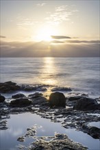 View of the sunrise over the Atlantic. Dreamlike clouds and a bay with a stone beach on a volcanic